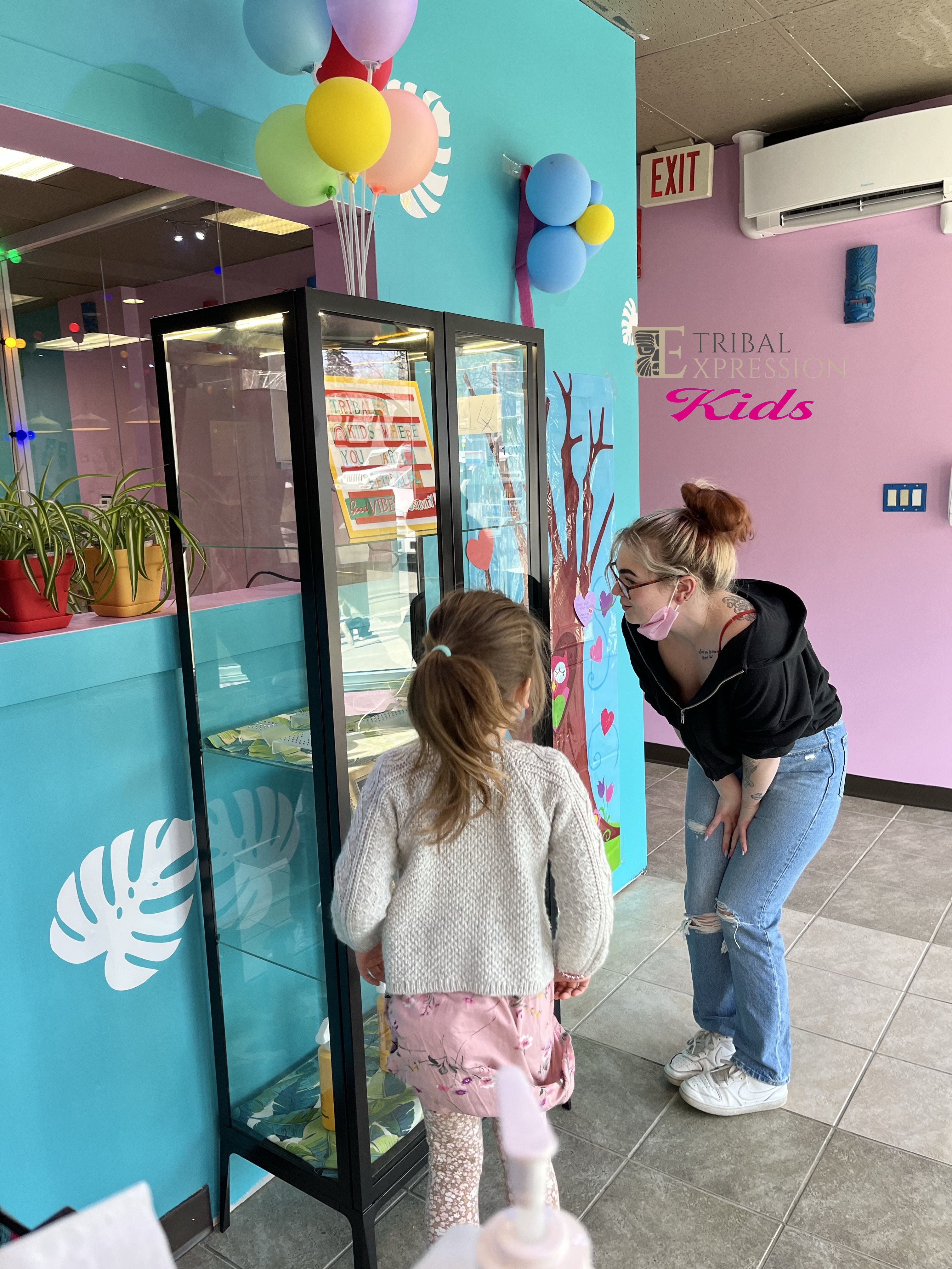 A child exploring the jewellery display case in the colourful Tribal Expression Kids studio with balloons on the wall