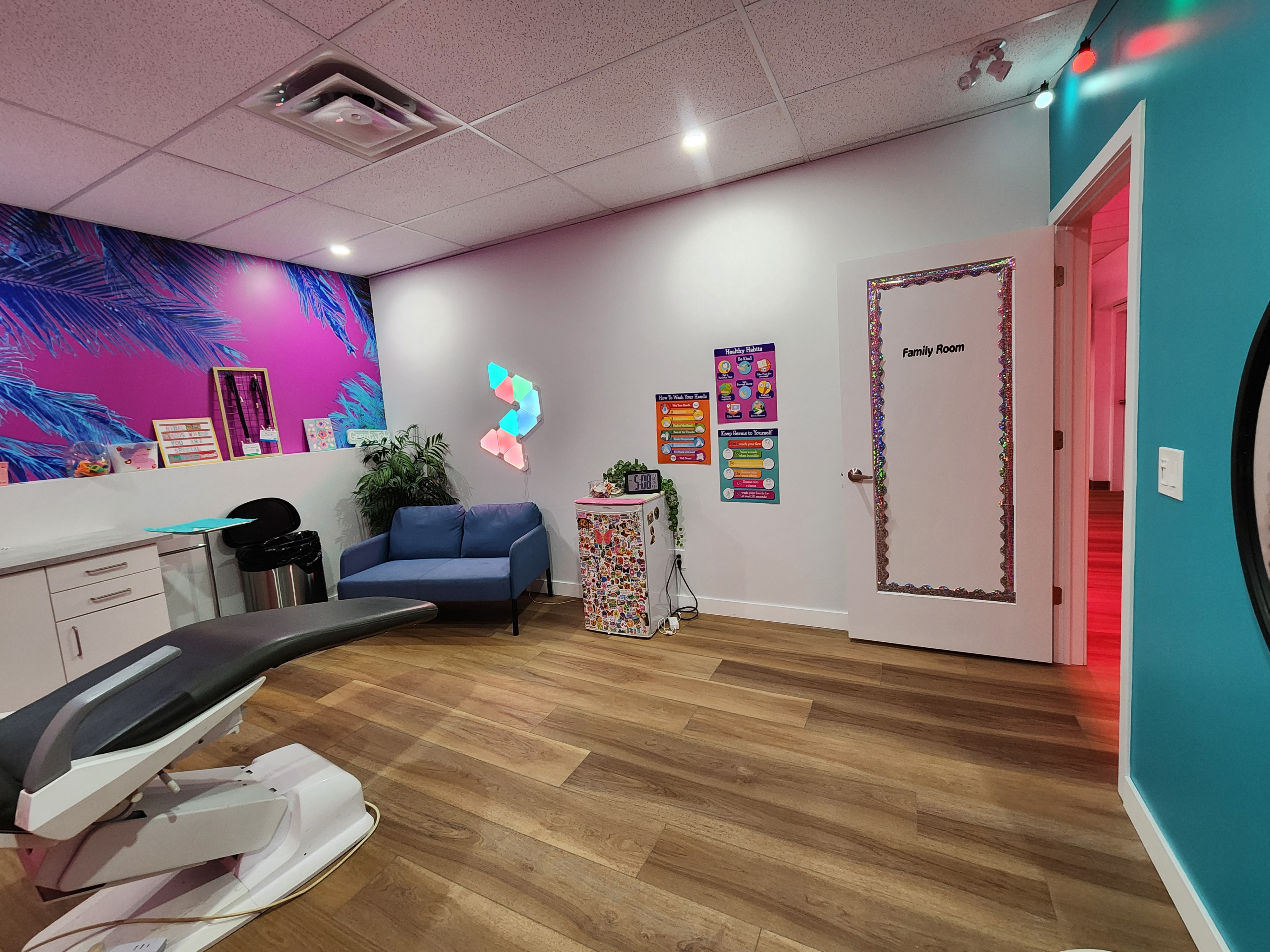 The Tribal Expression Family Room — a blue loveseat under a tropical mural with colourful geometric light panels, made just for kids.