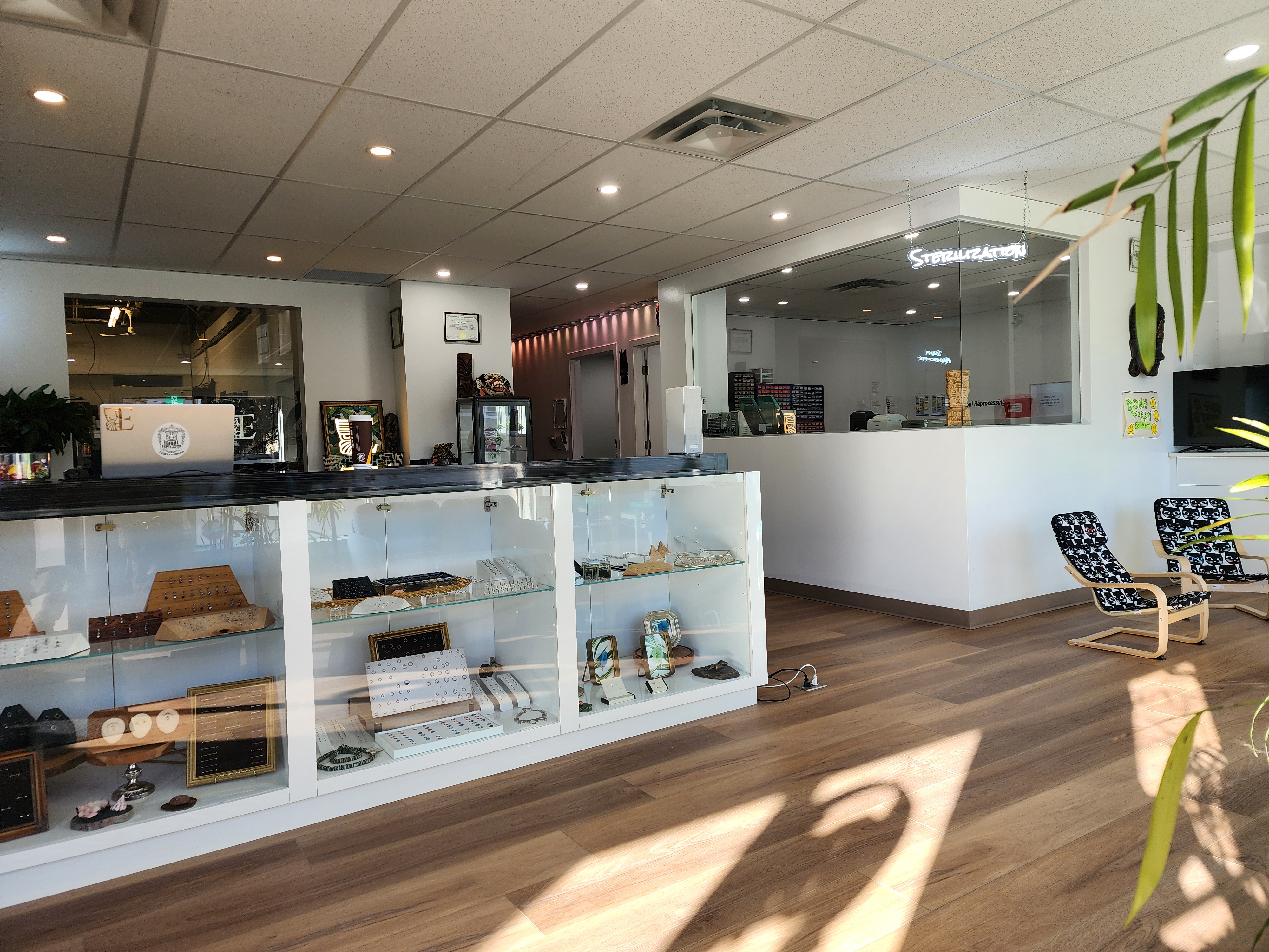 The main showroom of Tribal Expression in Calgary — jewellery display cases with earrings, kids seating, and the glass-walled sterilization room with its glowing STERILIZATION neon sign.