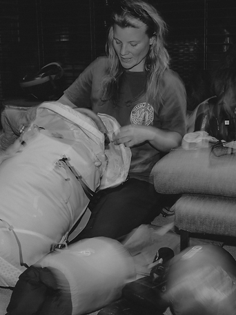 A woman kneeling and folding a lightweight duffel on the carpeted floor
