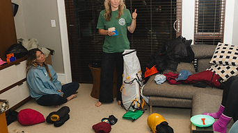 A group of women surrounded by packed gear and a standing white ultralight pack, thumbs up