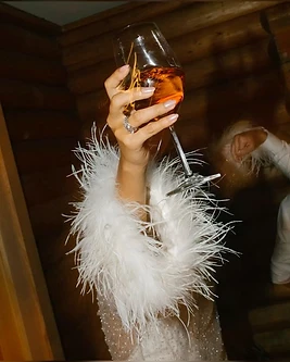 A hand raising a glass with feather trim
