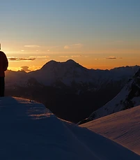 A skier silhouetted against a sunset over the Tantalus Range