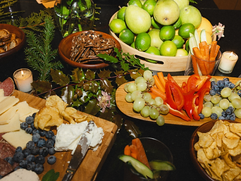 A festive charcuterie and snack spread with fruit, crackers, and candles on a dark surface