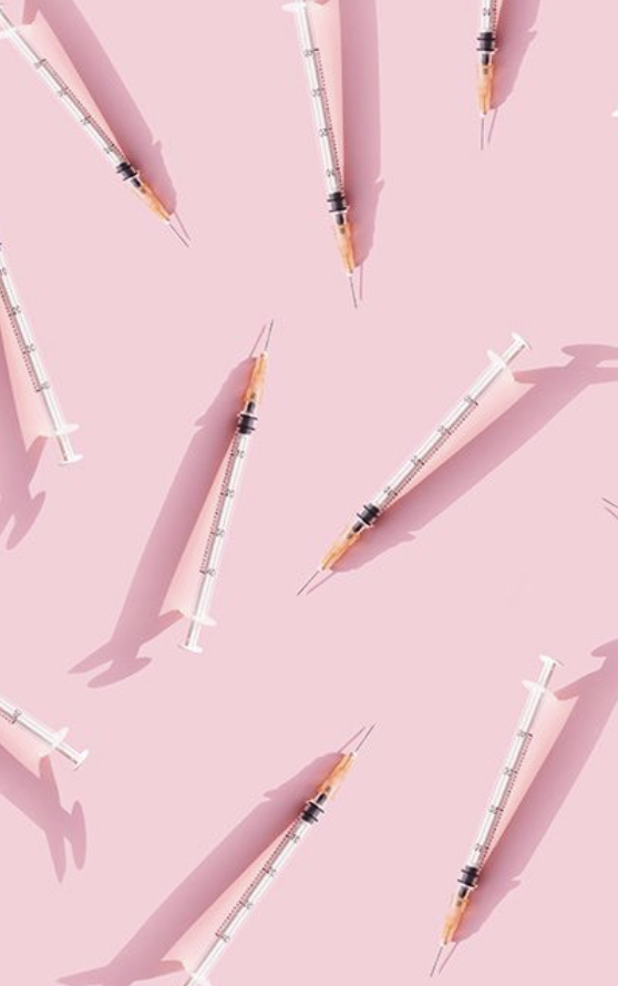 Flat-lay of medical syringes arranged on a soft pastel-pink surface