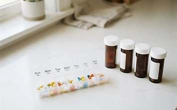 Weekly pill organizer and prescription bottles on a white countertop