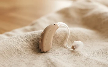 Discreet behind-the-ear hearing aid resting on soft neutral fabric