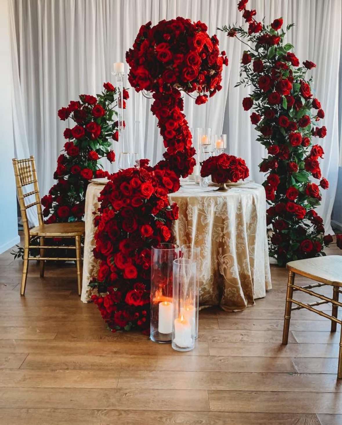 Romantic table setting with deep red roses, gold chairs, and candlelight