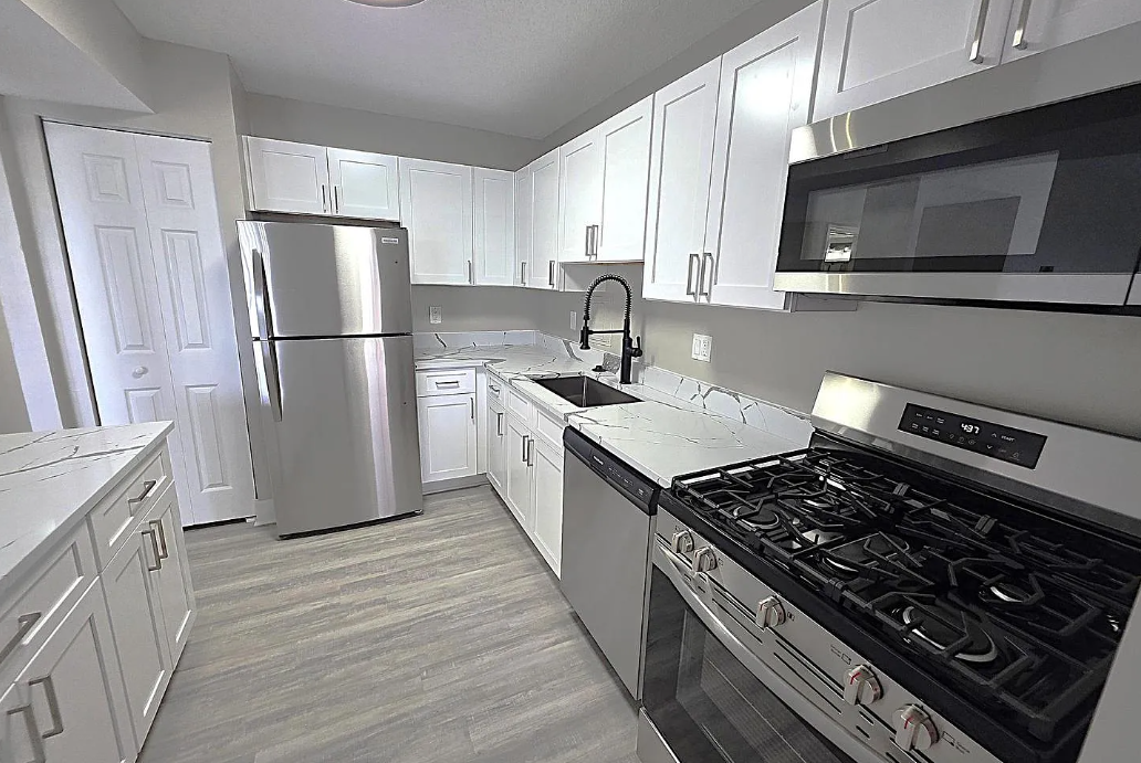 L-shaped white shaker kitchen with quartz counters and grey wood-look flooring
