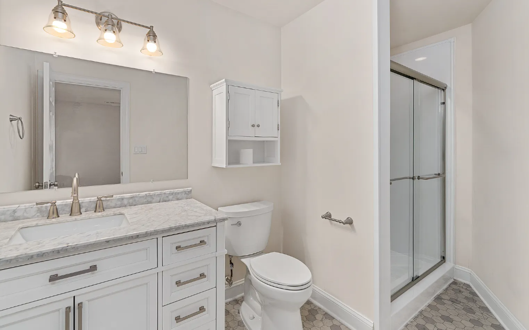 White vanity with brass hardware, medicine cabinet and glass shower with hex floor