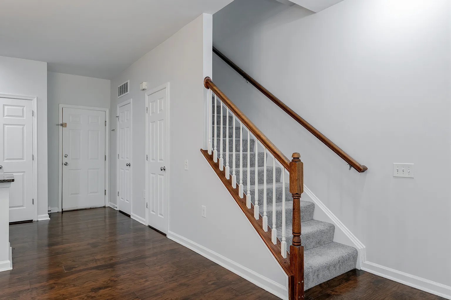 Staircase with wood handrail, white balusters and grey carpet runner