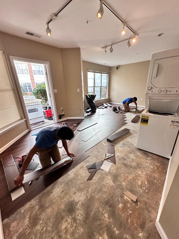 Crew installing dark wood-look plank flooring with subfloor exposed