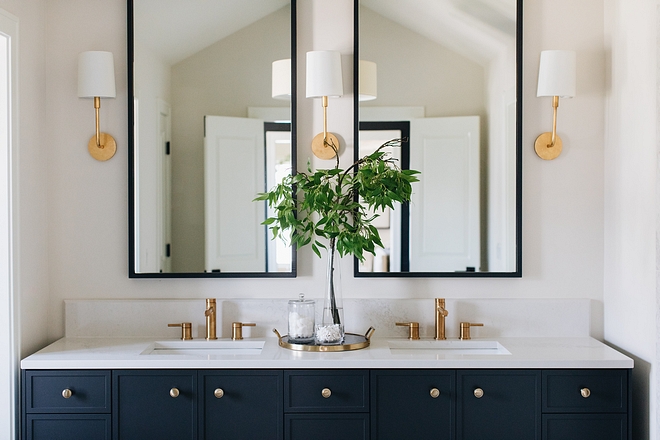 Navy double vanity with brass faucets, black-framed mirrors and sconces