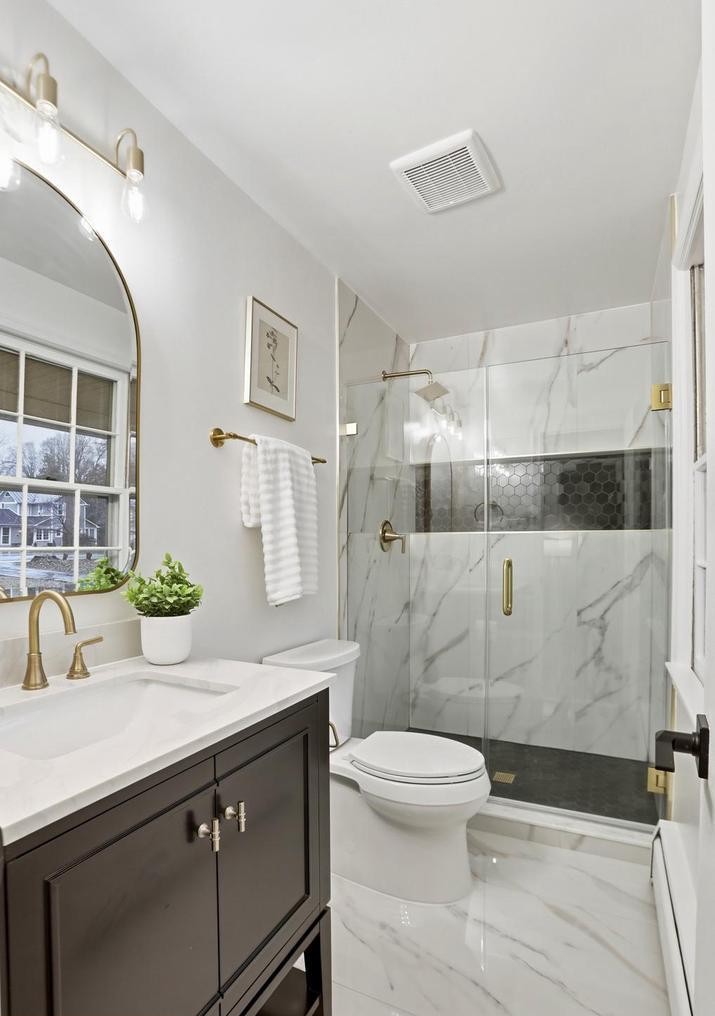 Modern bathroom with espresso vanity, arched gold mirror and marble shower with black hex accent