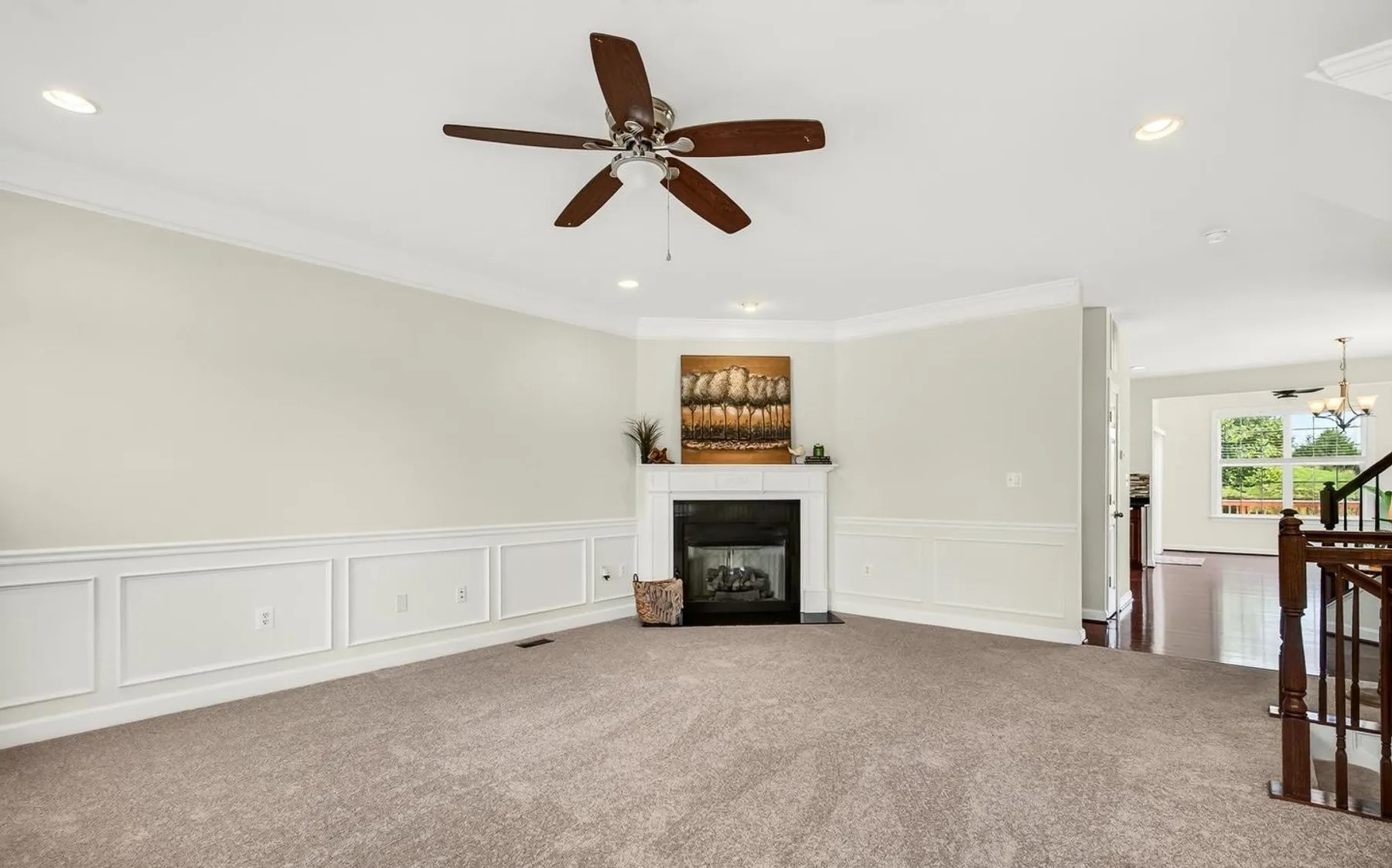 Carpeted living room with white fireplace, wainscoting and autumn landscape art