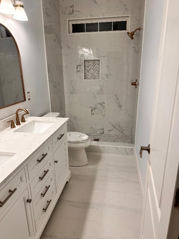 White shaker vanity with brass fixtures, arched mirror and herringbone-niche shower