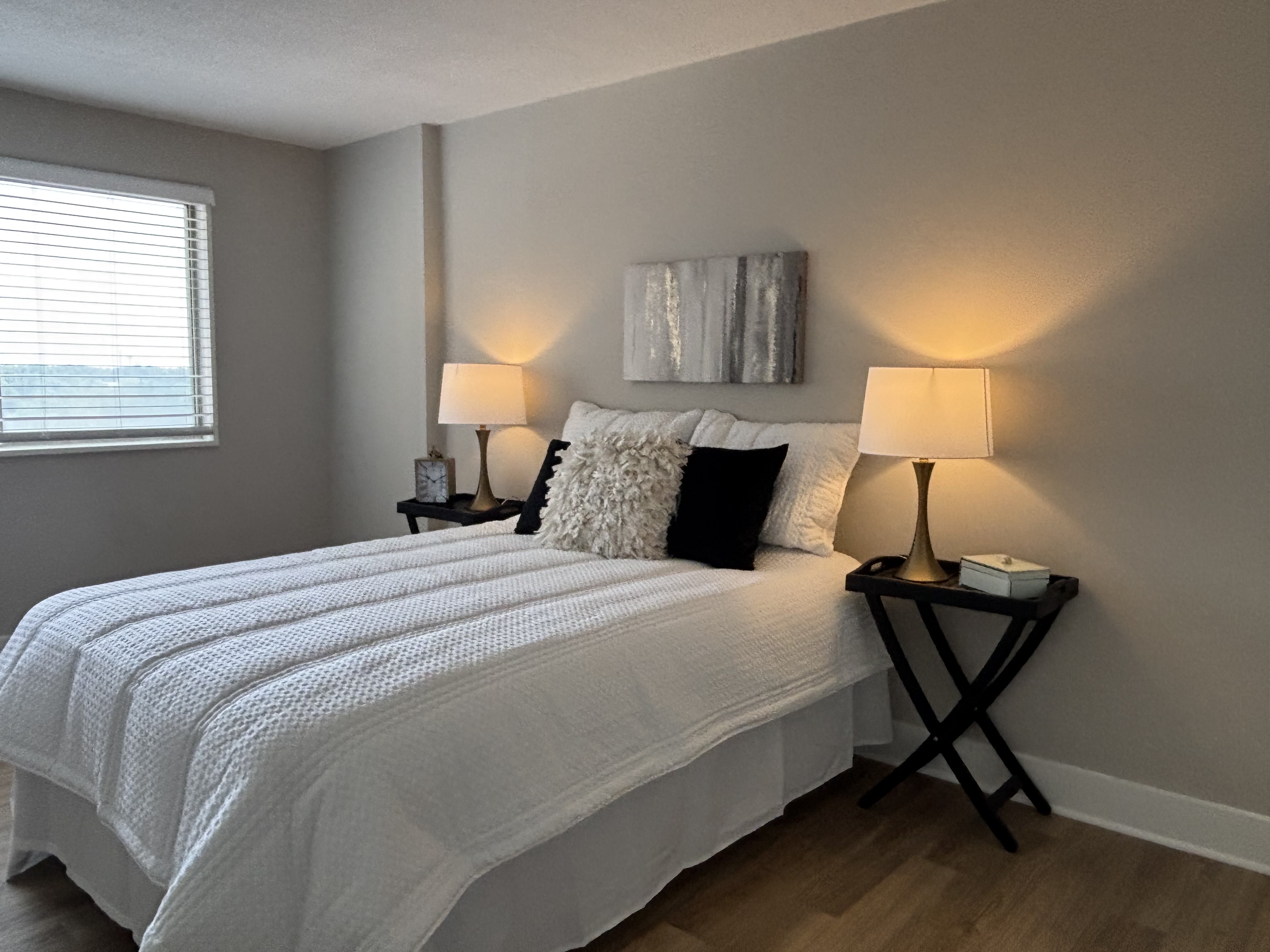 Bedroom with white bedding, black accent pillows, brass lamps and abstract art