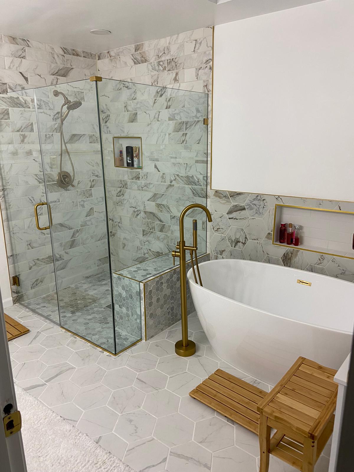 Wet room with glass shower, freestanding tub, gold fixtures and marble hex floor