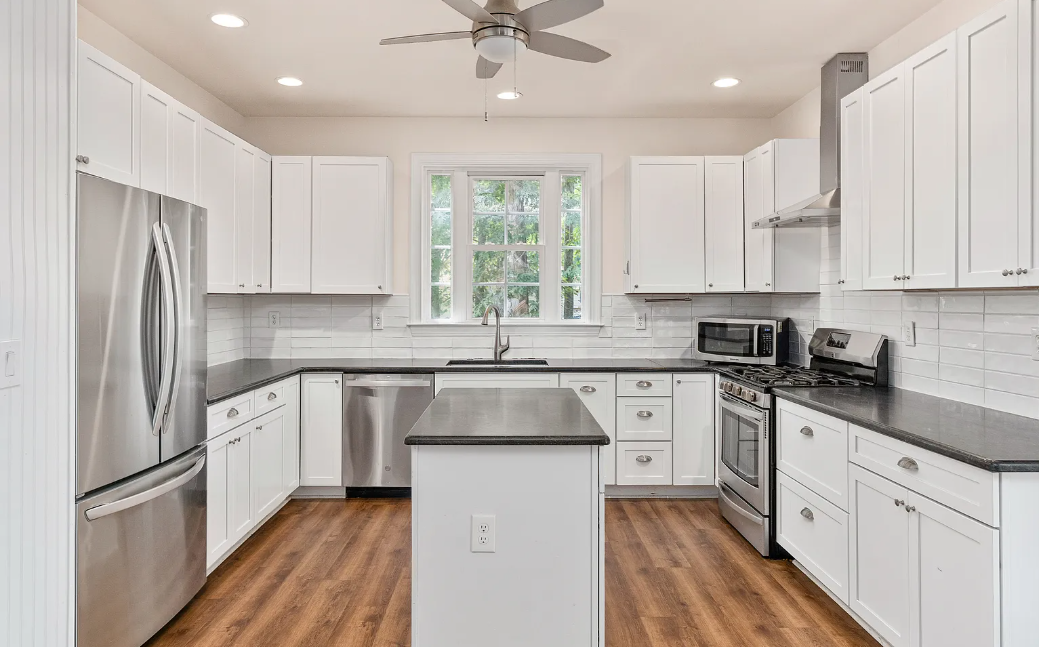 U-shaped white shaker kitchen with black island, subway tile and ceiling fan