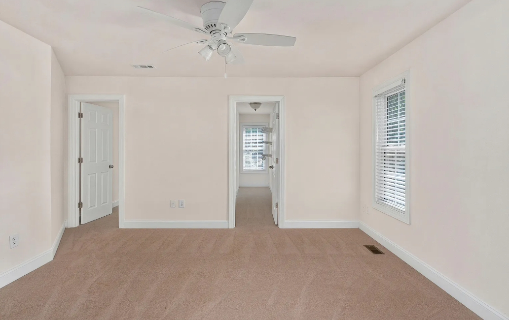 Vacant bedroom with beige carpet, ceiling fan and walk-in closet