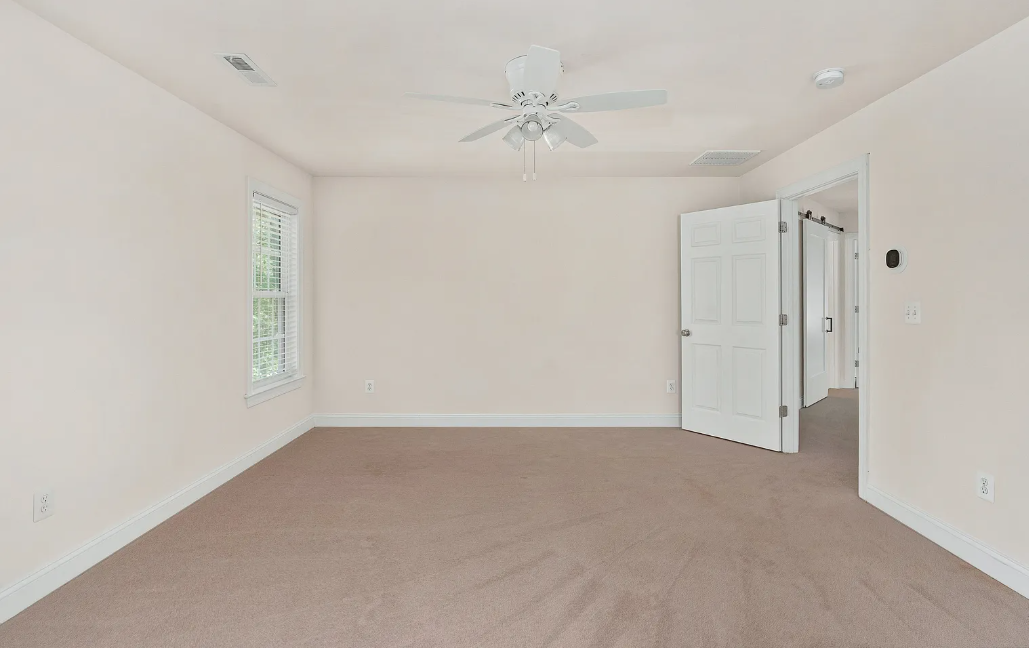 Minimalist bedroom with taupe carpet, ceiling fan and barn door to adjoining room