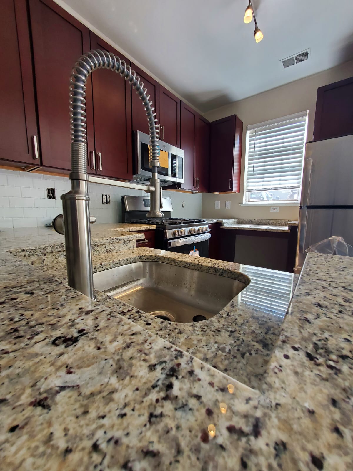 Cherry cabinetry kitchen with granite counters, subway tile and spring faucet