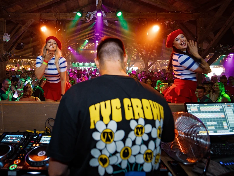 BRIAN performing behind the DJ booth, facing the crowd with stage lights