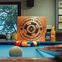 Engraved Winner's Circle plaque on the pool table beside canned drinks