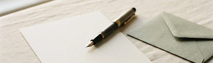 Fountain pen resting on a blank card beside a sage-green envelope in soft morning light