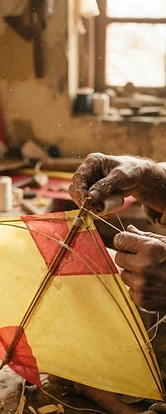 An artisan crafting a traditional yellow paper kite with bamboo and cotton thread