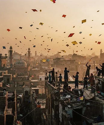 Colorful paper kites filling a warm amber sky above Lahore rooftops at golden hour