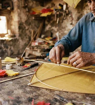 An artisan assembling a yellow paper kite with bamboo and cotton thread