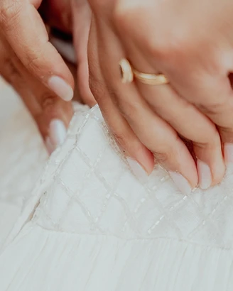 Hände mit goldenem Ring und Armband ruhen auf besticktem Brautkleid-Stoff