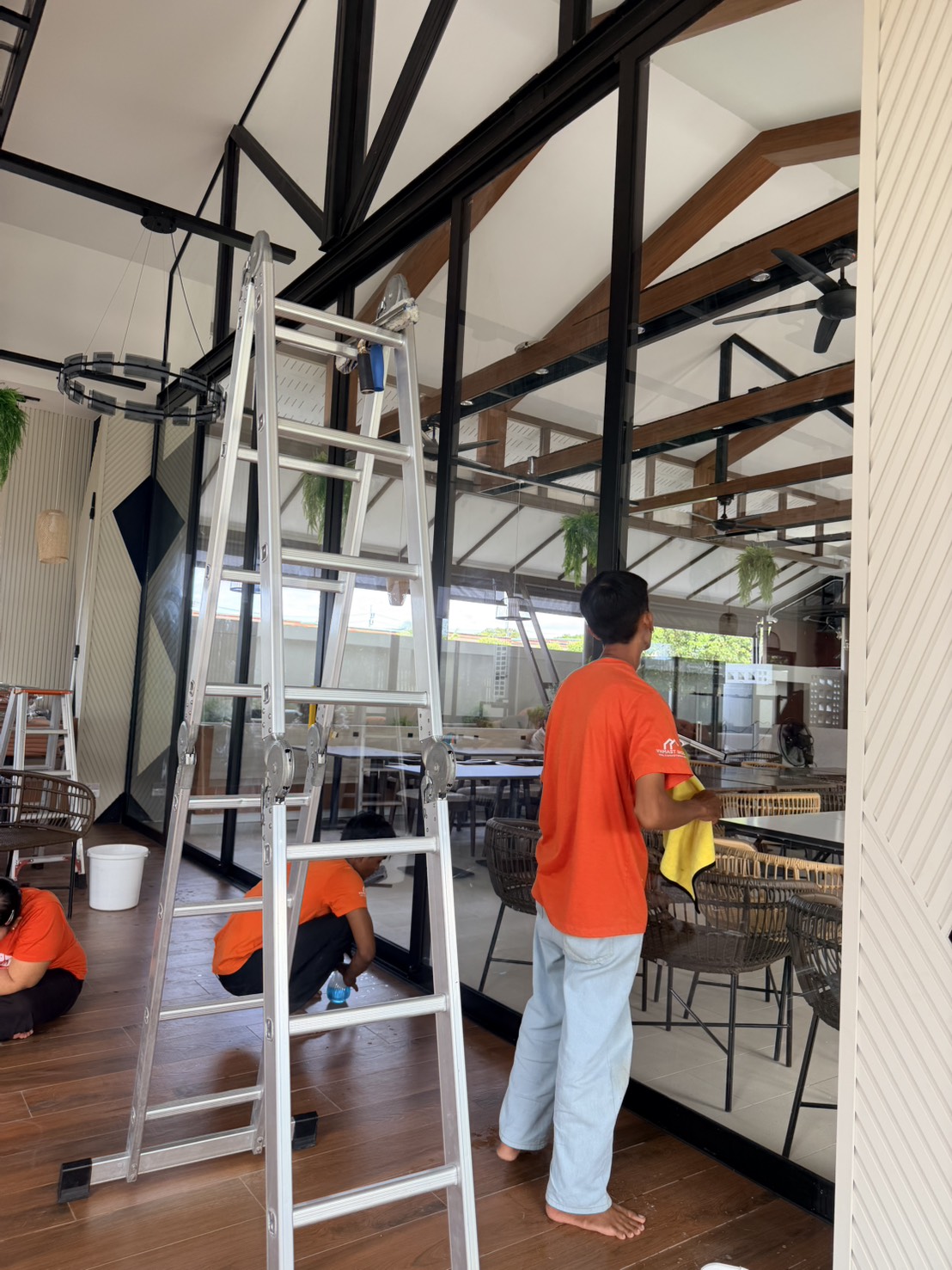 Crew member cleaning tall glass doors with a ladder