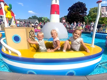 Three children enjoying a boat ride at Peppa Pig World, smiling in a yellow and blue boat on the water