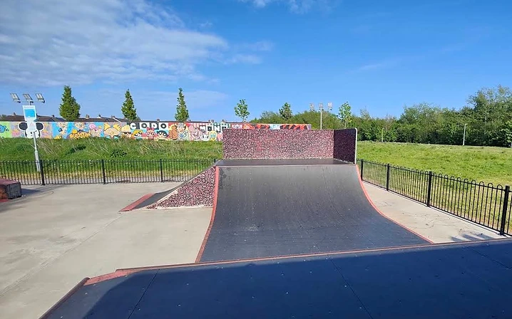 A quarter-pipe ramp at Comber Skate Park, with the concrete park, fence and a graffiti wall behind it