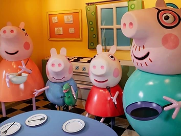 The Peppa Pig family brought to life indoors — Mummy Pig, George, Peppa and Daddy Pig in their kitchen at Peppa Pig World