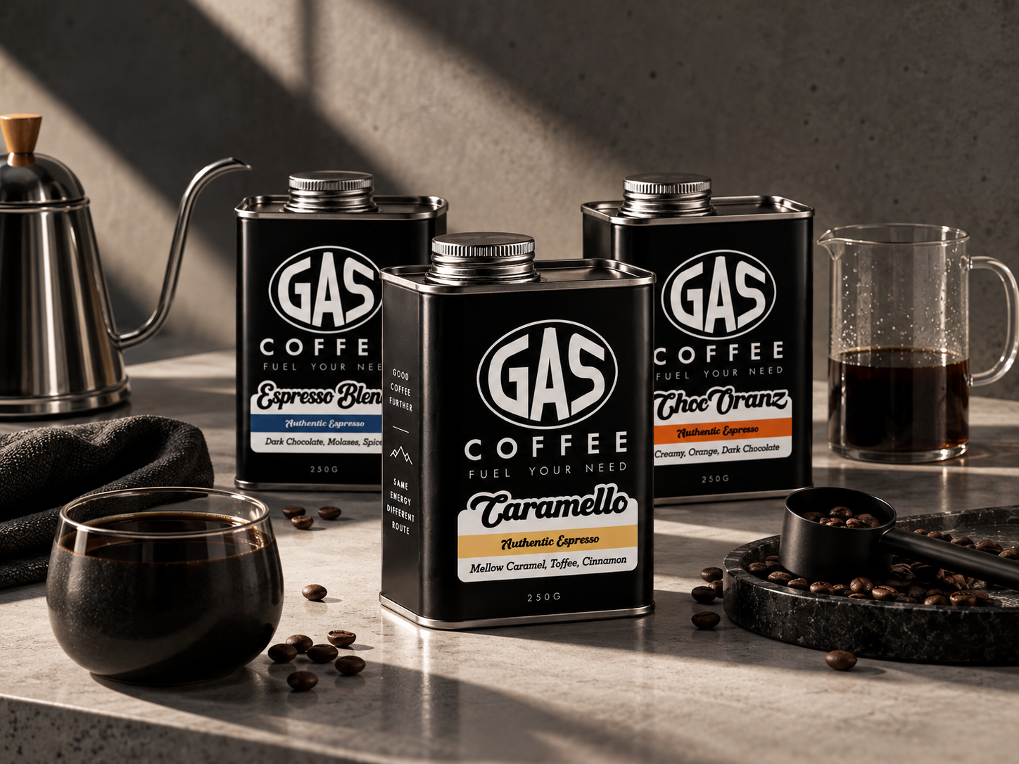 Three GAS Coffee tins — Espresso Blend, Caramello and Choc-Oranz — on a stone surface with brewing props
