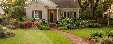 Goose Creek front yard with lush green grass, in-ground irrigation sprinkler, azaleas, hydrangeas, brick walkway, and mature oak trees