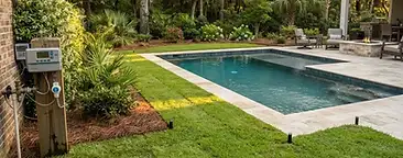 Completed residential swimming pool with a professionally installed irrigation system in a South Carolina Lowcountry backyard, pop-up sprinkler heads visible in the lawn but not spraying