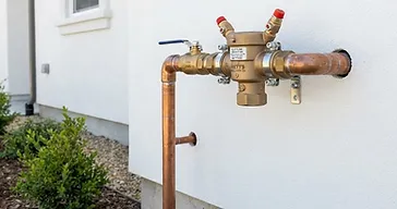 Backflow preventer device installed on an exterior house wall with copper and brass piping connections