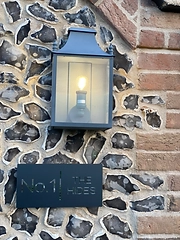 Black metal No.1 The Hides sign mounted on a flint wall beneath a lit lantern