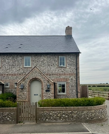 Flint and brick front facade with an arched porch and lanterns flanking the door