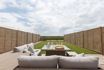 Patio with a wicker sofa, glass-topped table and a long lawn stretching to the horizon