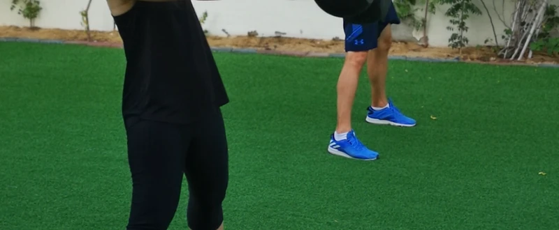 Two clients performing kettlebell swings on outdoor turf with Nick