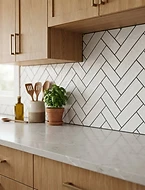 Finished kitchen tile backsplash in herringbone pattern with warm wood cabinets