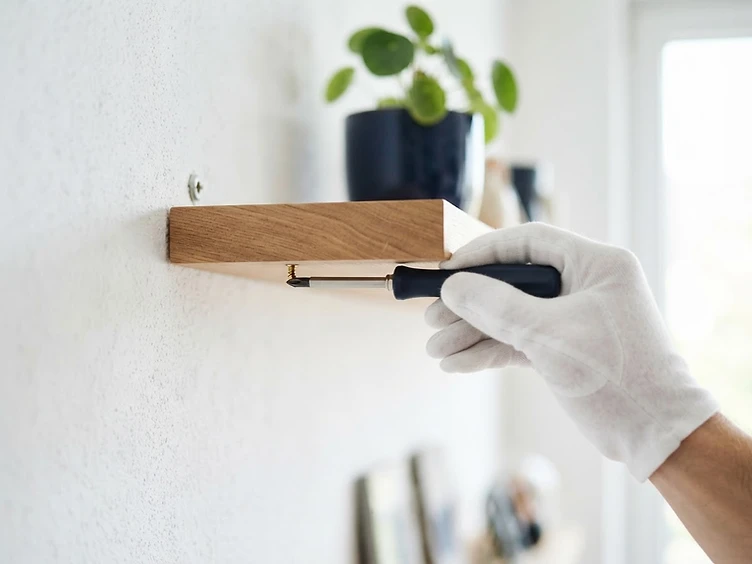 A white-gloved hand holding a screwdriver near a mounted shelf