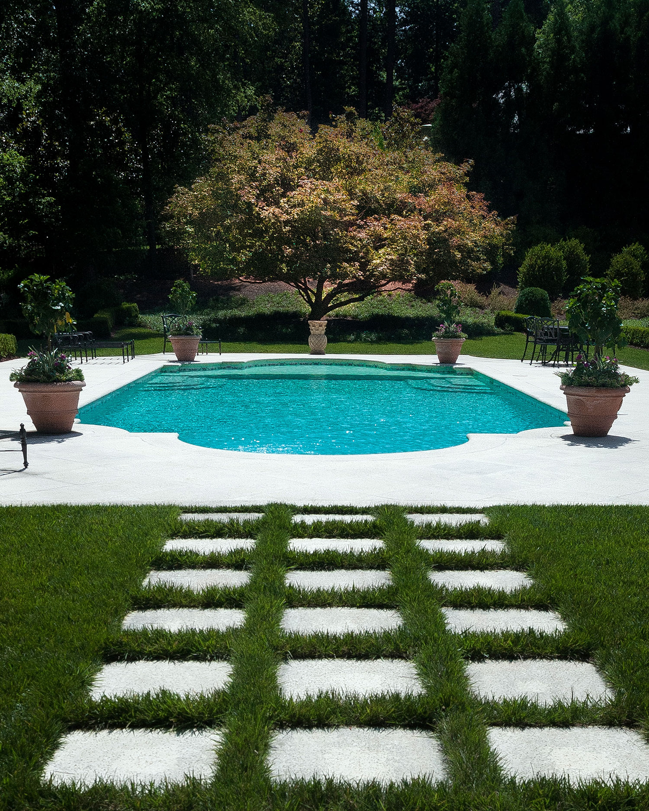 Stone stepping pads in lawn leading to a pool with urns and a flowering tree beyond