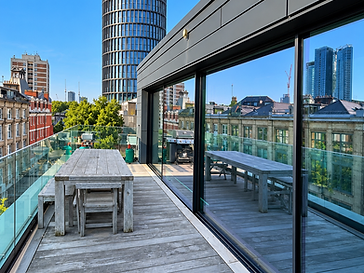 Urban balcony with a large floor-to-ceiling minimal-frame sliding glass wall system in black frames, reflecting a London city skyline