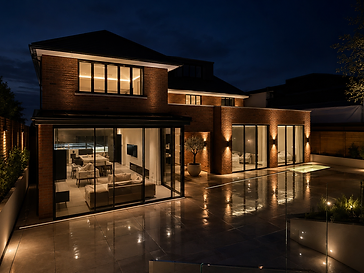 Night-time rear facade of a detached two-storey brick residence with extensive floor-to-ceiling minimal-frame sliding glass doors over a reflective stone patio